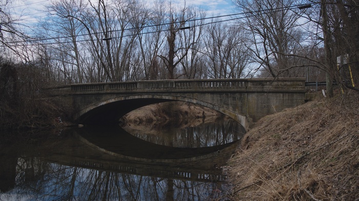 Concrete arch bridge over a calm river with bare trees