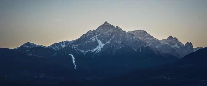 Snow-capped mountains at sunset with a contrail