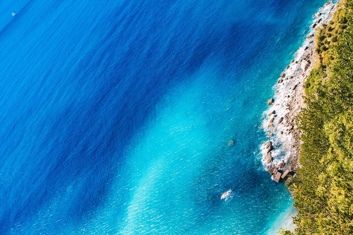 Aerial view of a rocky coastline with turquoise water and green trees