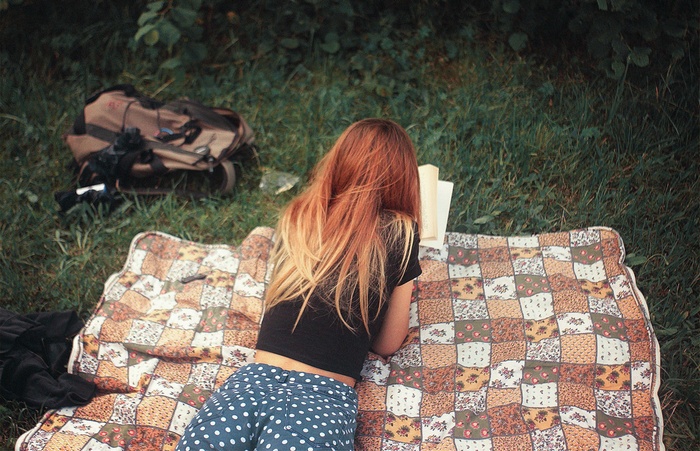Woman reading a book on a picnic blanket outdoors
