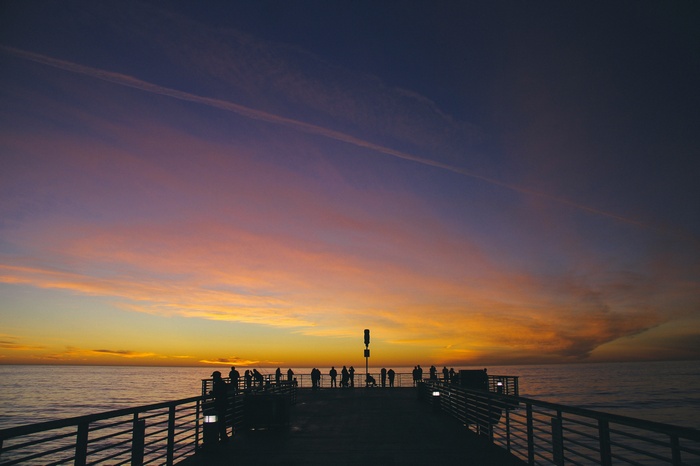 People on a pier watching a sunset over the ocean