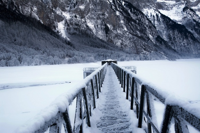 Snow-covered bridge over a frozen lake with mountains