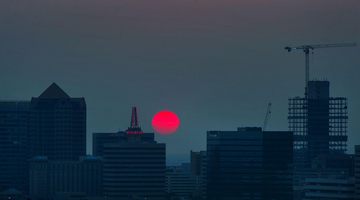 Cityscape with red sun setting behind buildings and construction cranes