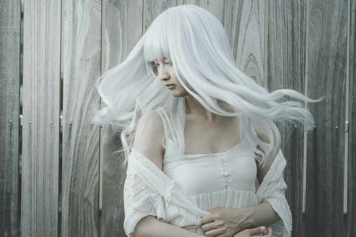 Woman with long white hair in front of wooden fence