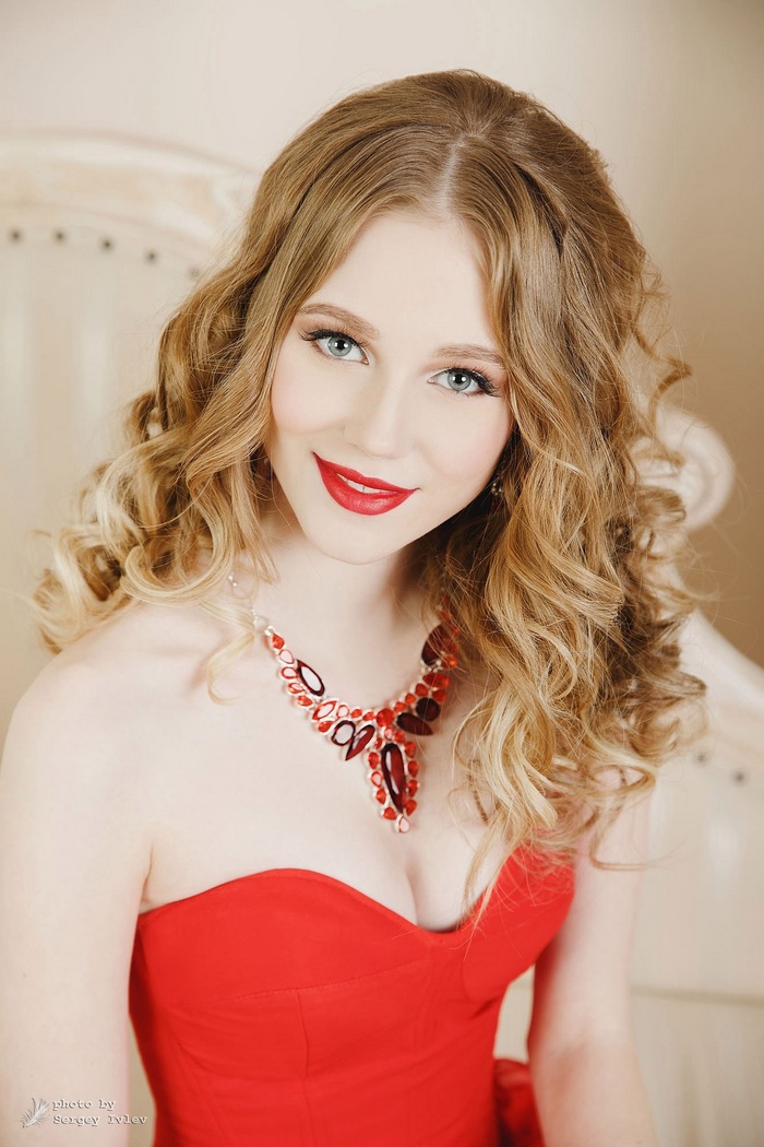 Woman with blonde curly hair wearing a red dress and necklace