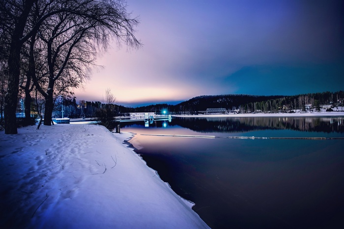 Winter landscape with snow-covered shore and calm lake at dusk
