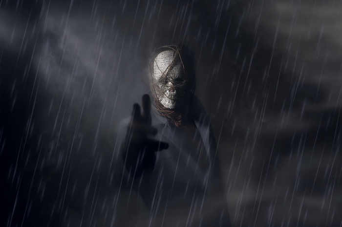 A figure with a masked face in the rain