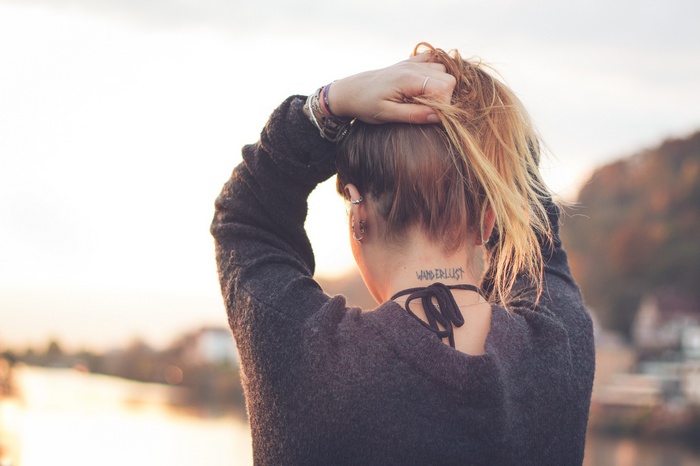 Woman with tattoo on neck, hands in hair outdoors