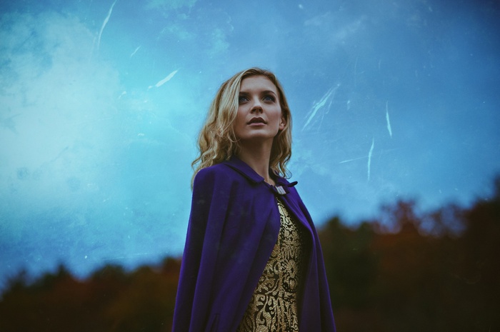Woman in purple cloak and gold dress looking up
