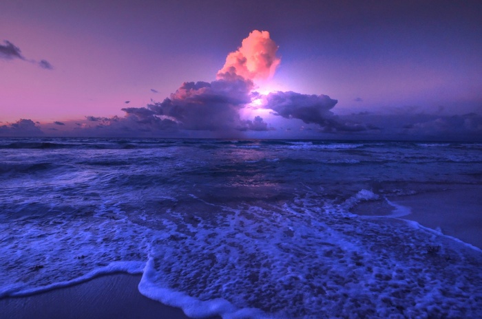 Ocean waves under a dramatic purple and pink sky with clouds