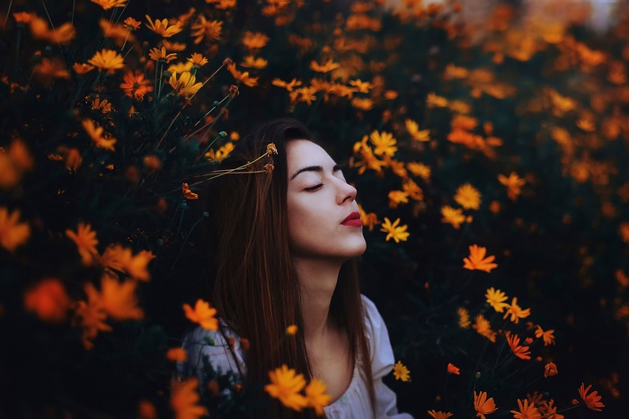 Woman with closed eyes surrounded by orange flowers