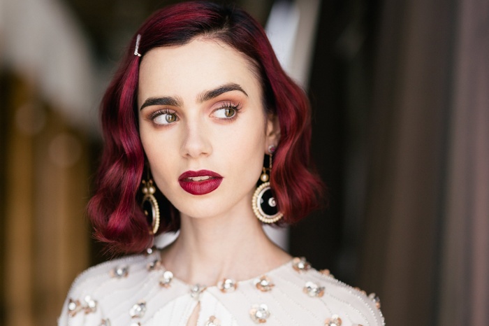 Lily Collins with red wavy hair and dramatic makeup