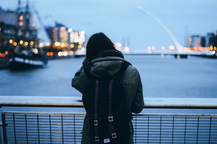 Woman with backpack looking at city lights across river