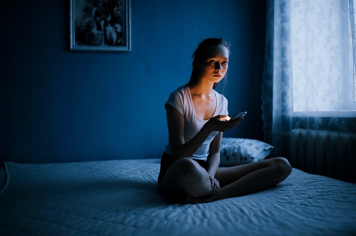 Young woman sitting on a bed with a smartphone
