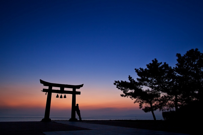 Silhouette of a man leaning on a Torii gate at sunset
