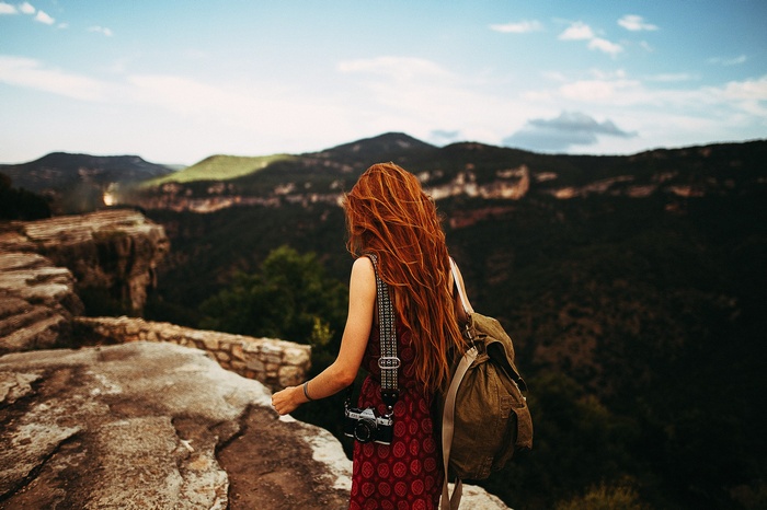 Woman with red hair and camera on cliff overlooking mountains