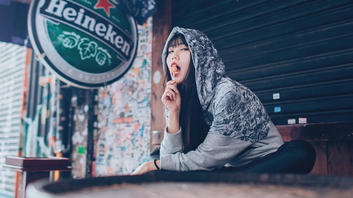 Asian woman with lollipop in front of Heineken sign