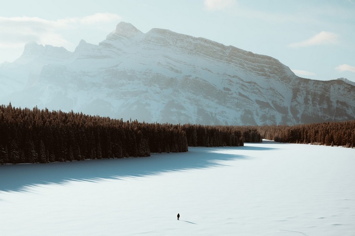 Person walking on a frozen lake with mountains and forest