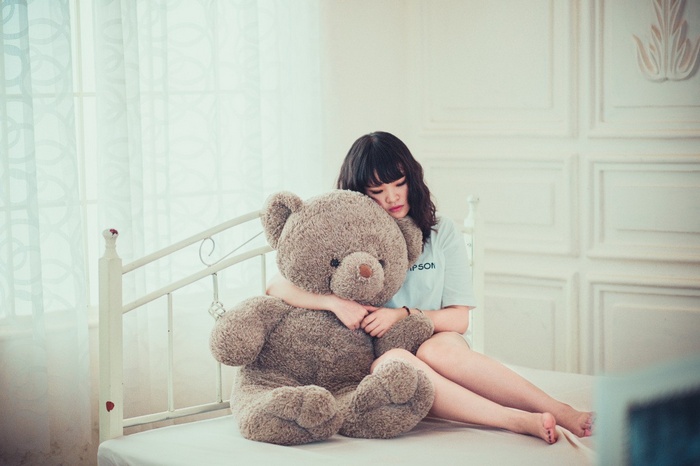 Young woman hugging a large teddy bear in bed