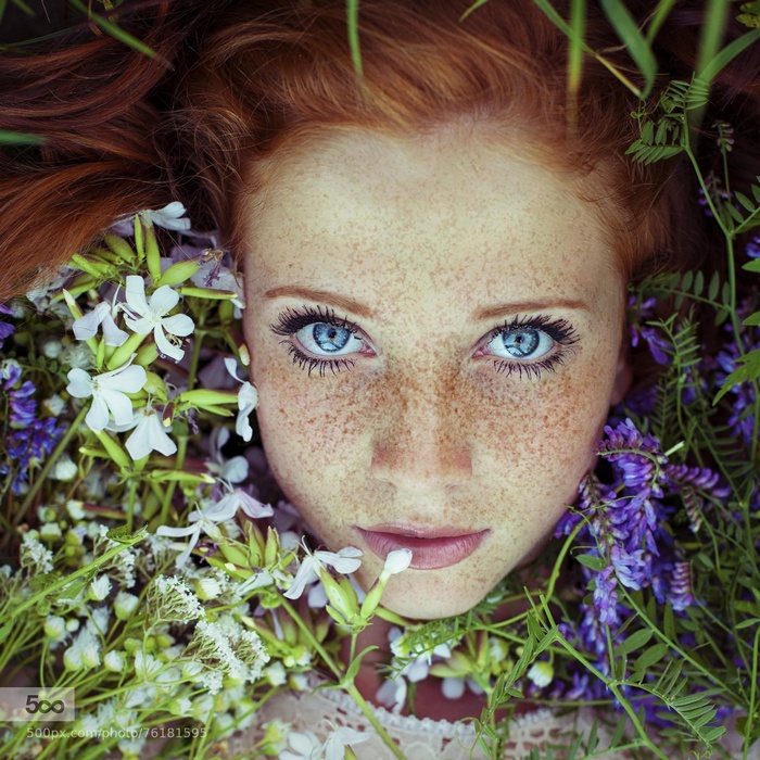 Redhead woman with freckles lying in flowers