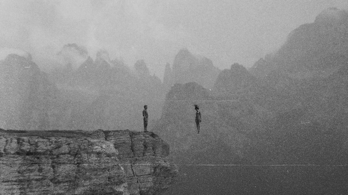 Two figures on a cliff edge with mountains in the background