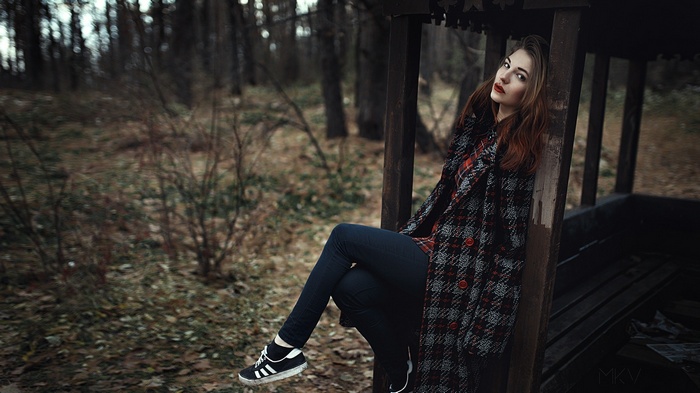Woman in plaid coat sitting in a wooden structure in a forest