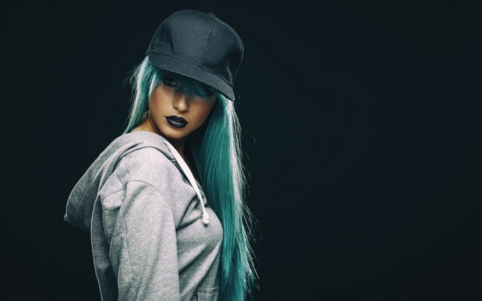 Woman with blue hair and black lipstick wearing a hat and hoodie