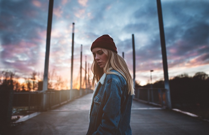 Woman wearing a beanie and denim jacket on a bridge at sunset