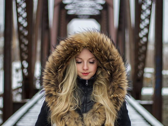 Woman with blonde hair and fur hood on a bridge