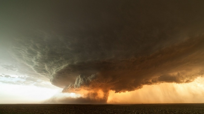 A massive tornado storm over a field at sunset