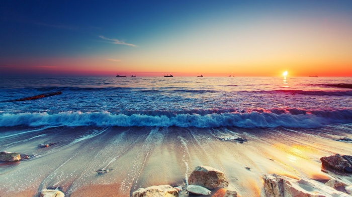 Sunset over the ocean with waves crashing on the beach