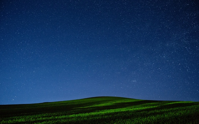 Starry night sky over a green hill