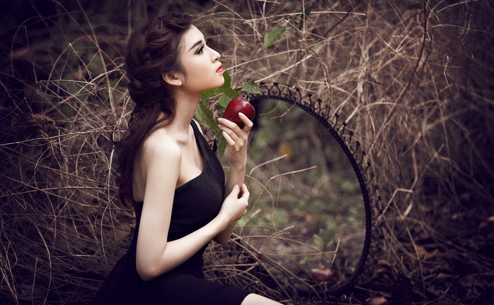 Woman in black dress holding an apple near a mirror