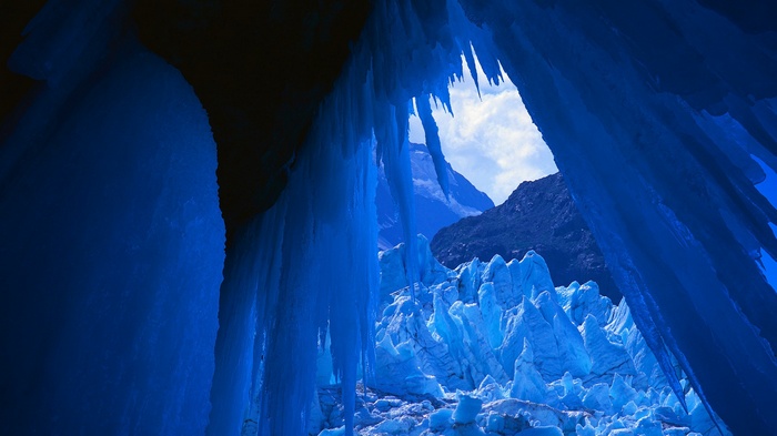 Icicles hanging over a glacier with mountains in the background