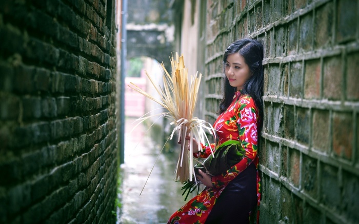 Woman in traditional dress holding reeds by brick wall