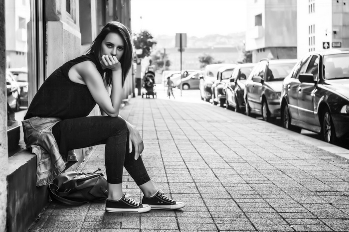 Woman sitting on sidewalk with cars in background