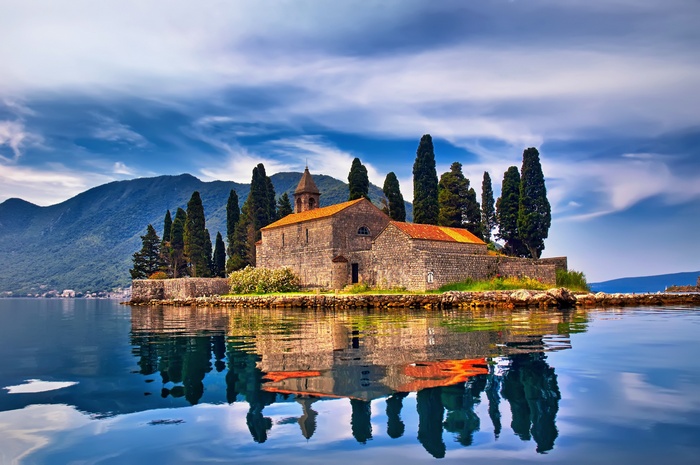 Island church with cypress trees and reflection in water