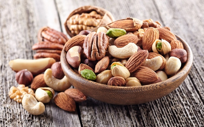 A wooden bowl filled with assorted nuts on a wooden surface