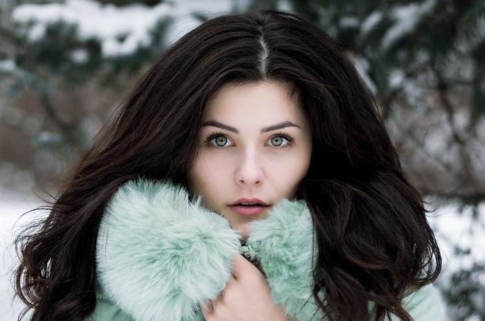 Woman with dark hair and green eyes wearing a fur-lined coat