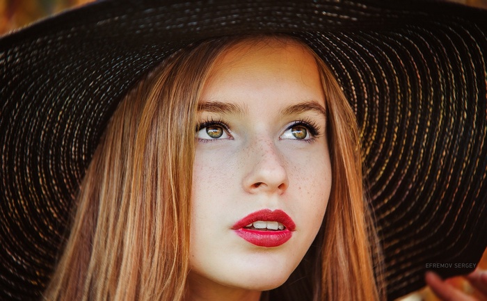 Woman with auburn hair wearing a black hat and red lipstick