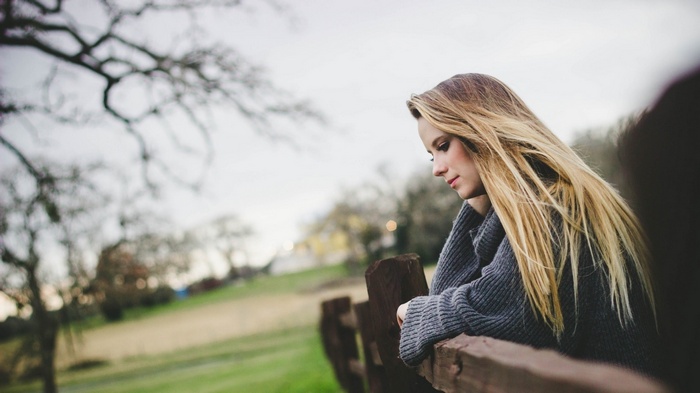 Woman with long blonde hair leaning on a wooden fence