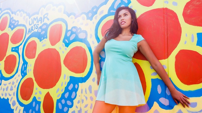Woman in a mint green dress posing against a colorful mural