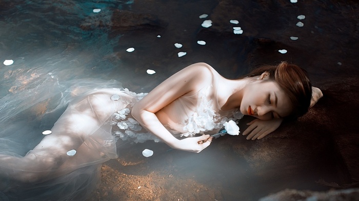 Woman in sheer dress with flowers lying in water
