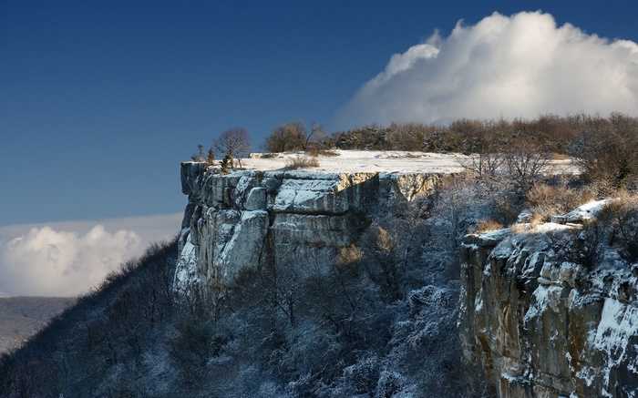 Snow-covered cliff overlooking a valley under a blue sky