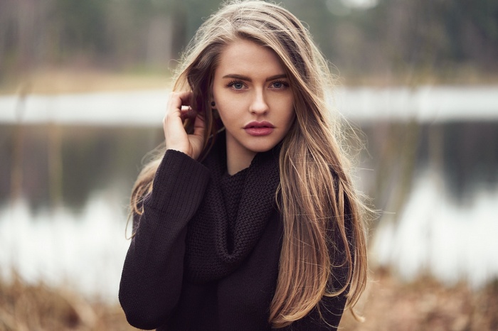 Woman with blonde hair wearing a black sweater and scarf