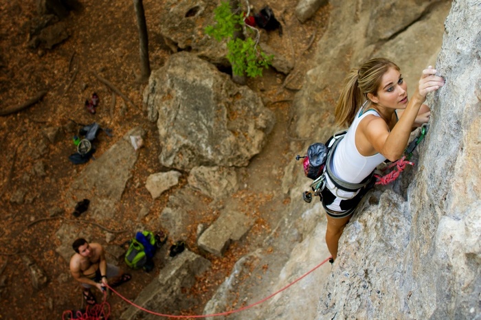 Woman rock climbing, man belaying below