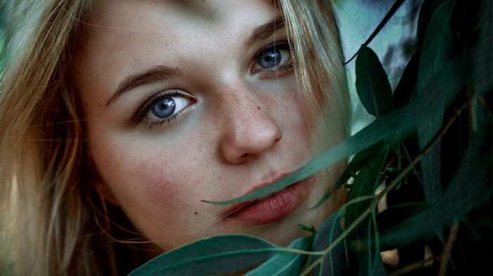 Young woman with blue eyes and freckles behind leaves