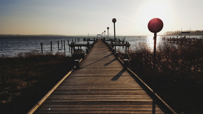 Wooden pier with lampposts and a bicycle sign at sunset