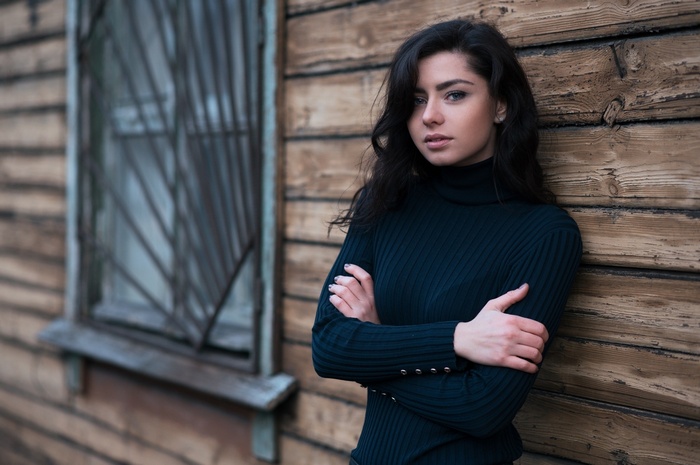 Woman with arms crossed leaning against a wooden wall