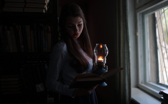 Woman reading a book by lantern light near a window